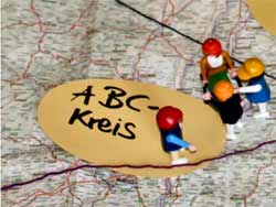 Playmobil-Männchen auf einer Landkarte und ein rundes Moderationskärtchen mit ABC-Kreis